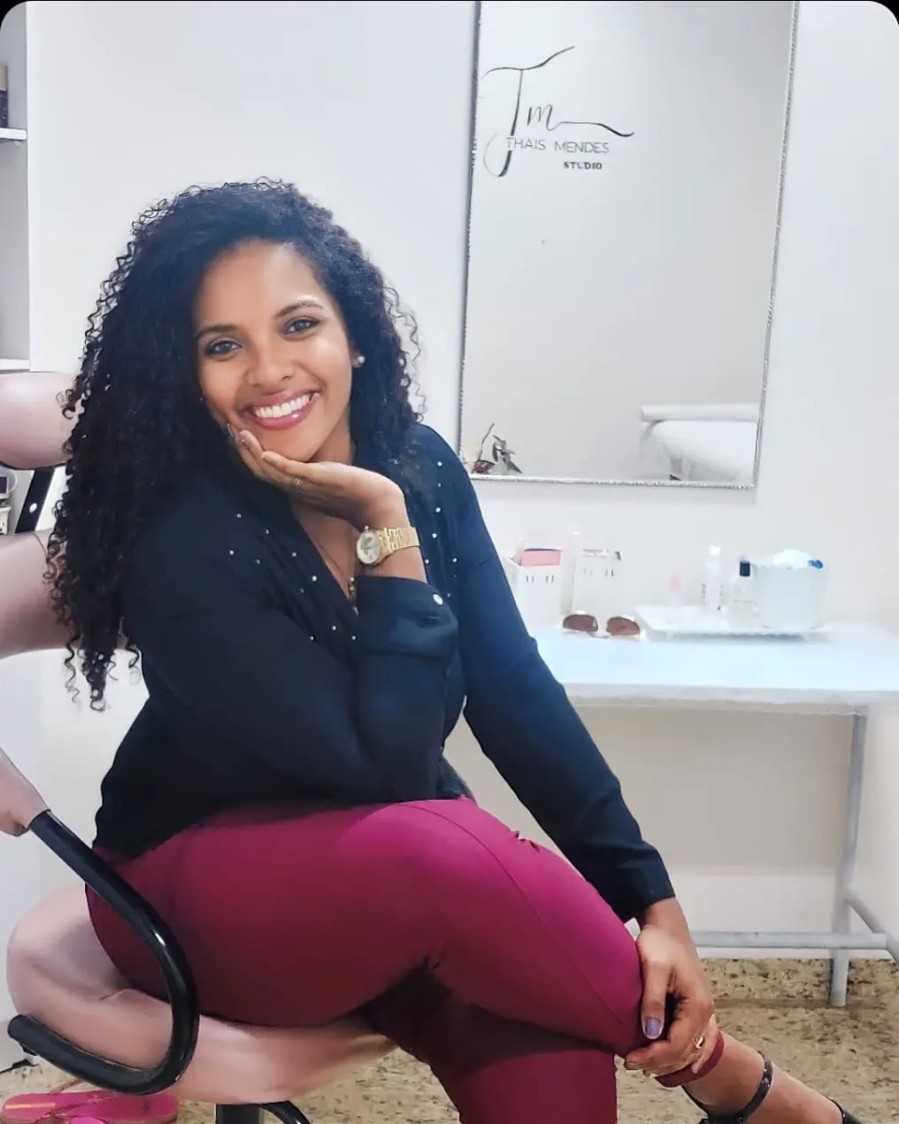 Thais Mendes sentada no espaço do estúdio, com o nome Thais Mendes Studio ao fundo